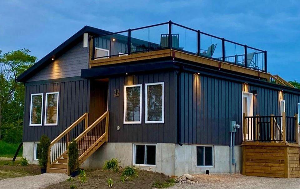 Modern two-story house with rooftop deck and wood accents, lit by several exterior lights.